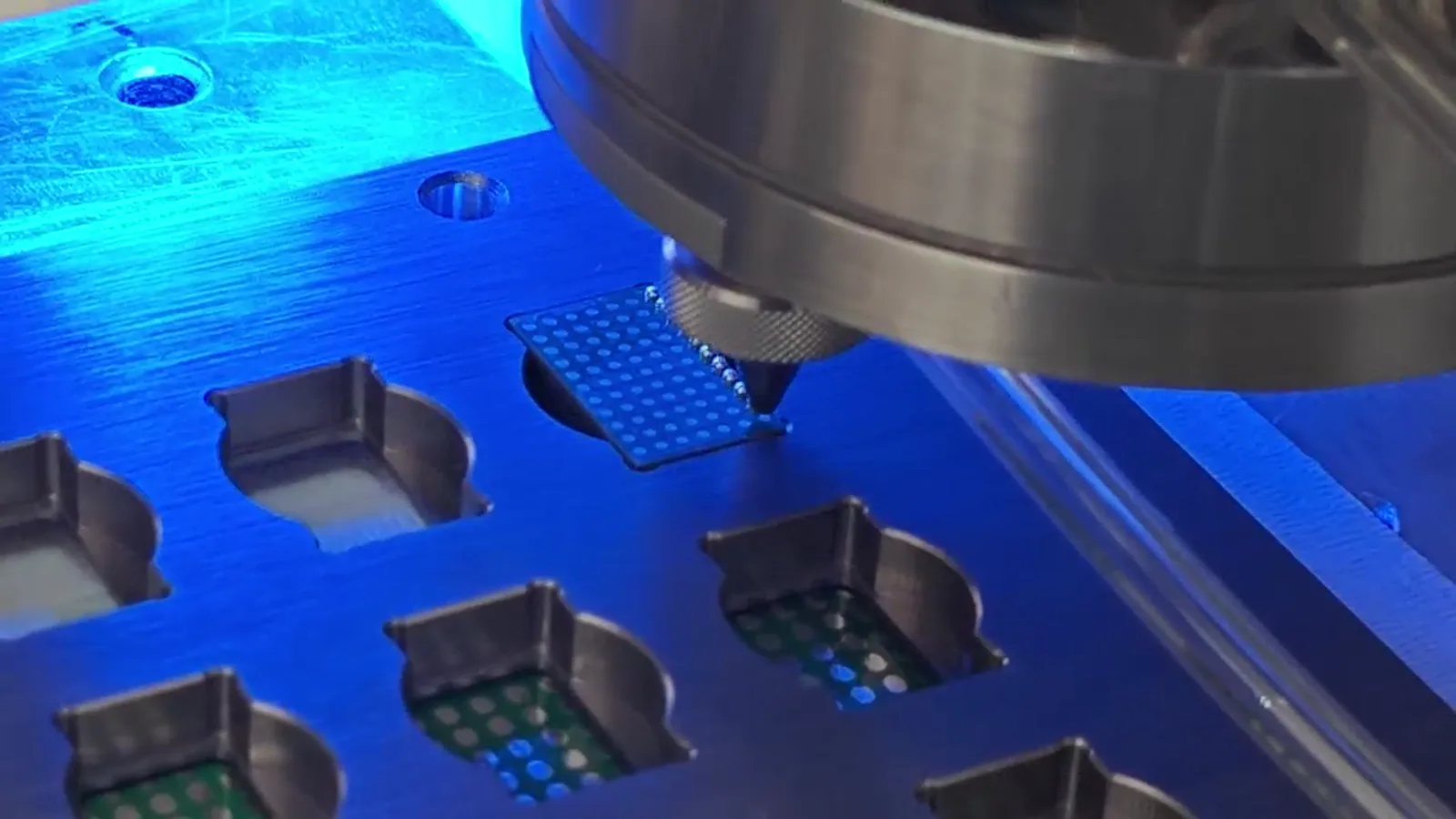 Supplied jetting head approaching a supported electronic workpiece in a blue fixture